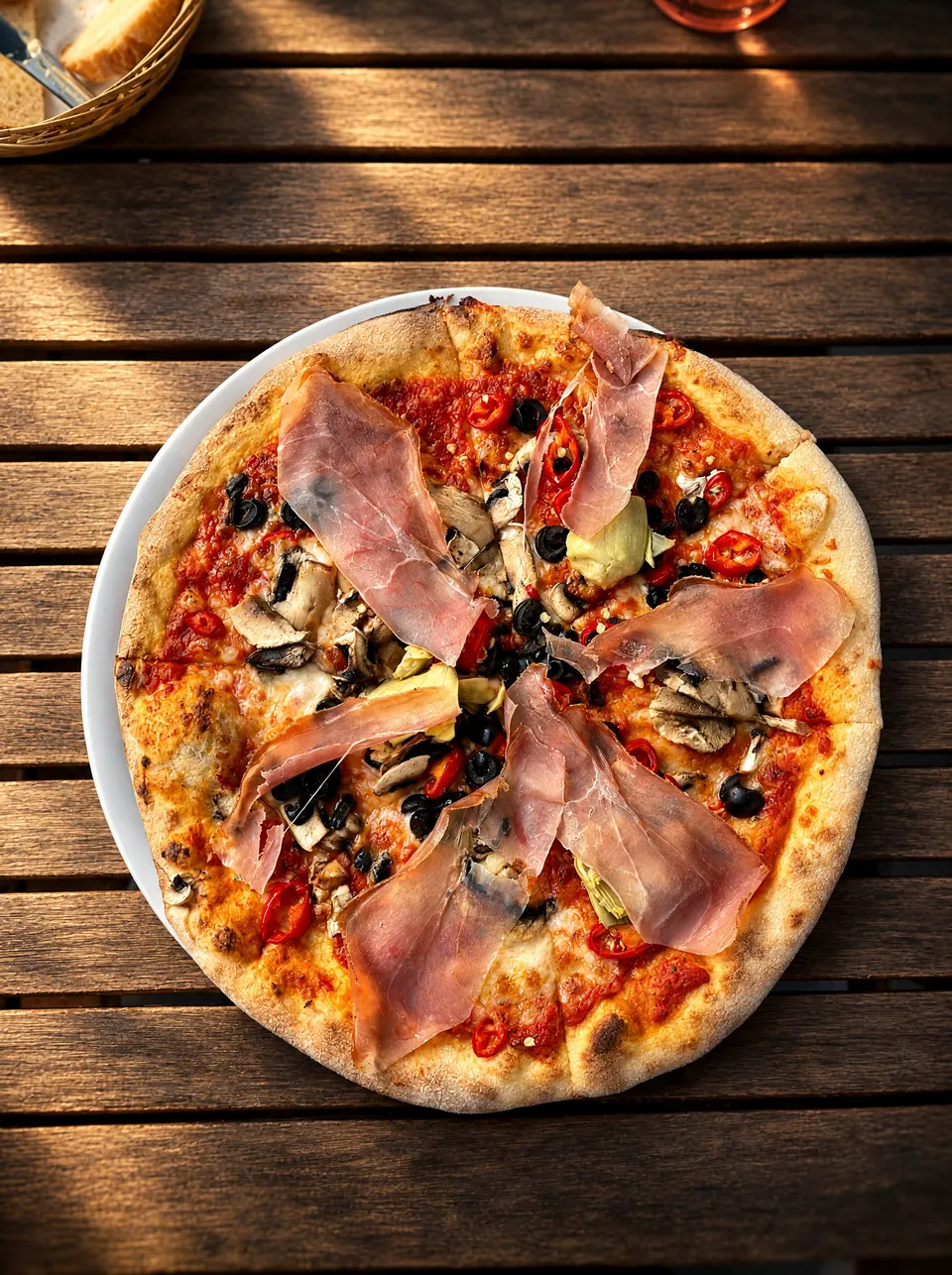 Pizza se šunkou, houbami a olivami na dřevěném stole