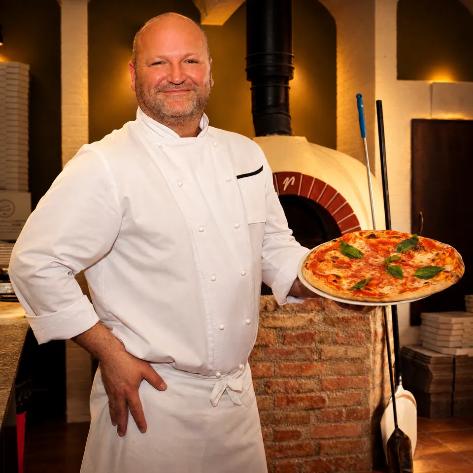 Pizzař s pizzou u pece v restauraci Trattoria Famiglia